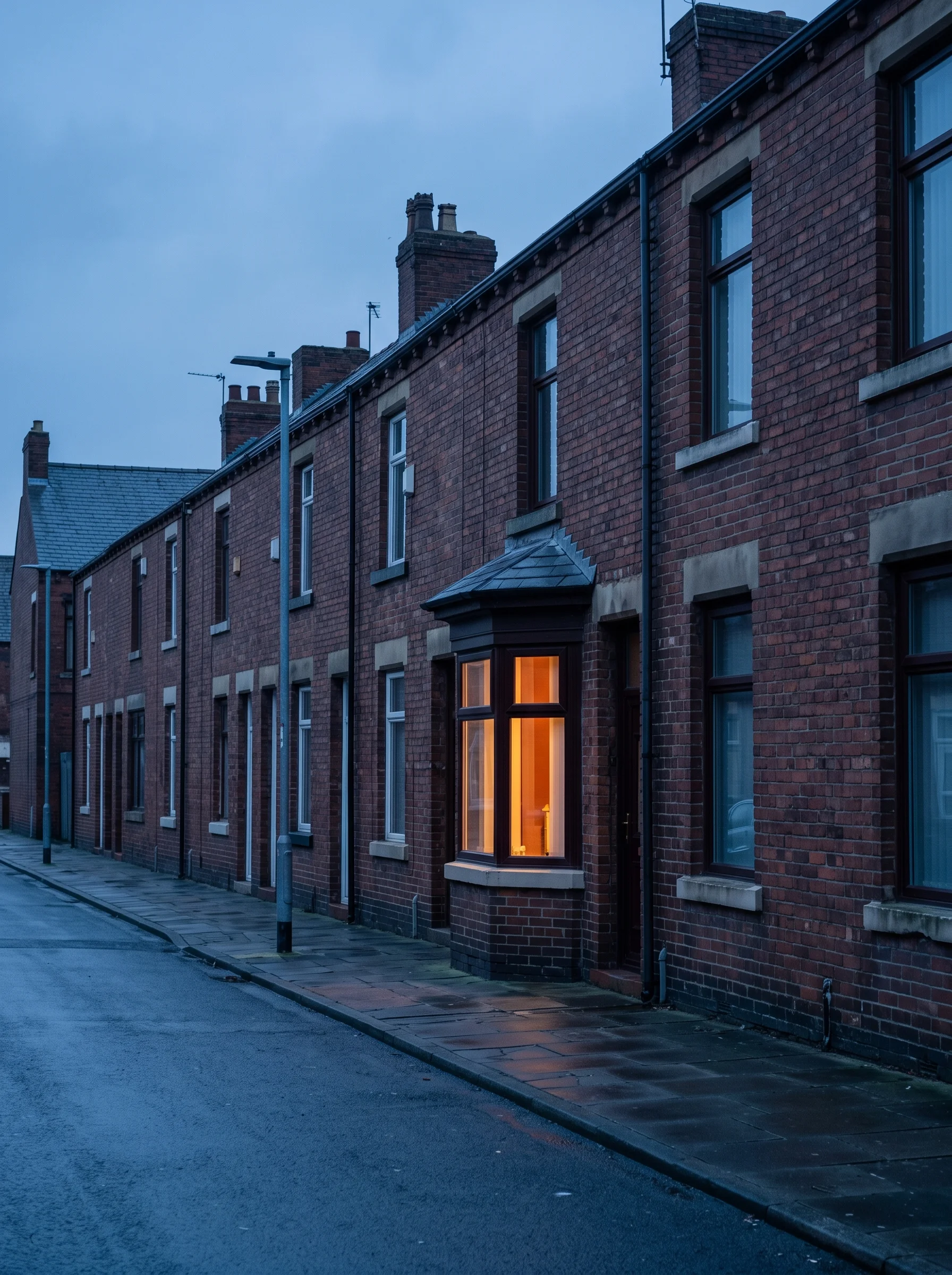 Victorian terrace street at dusk, cold and blue-grey, with one bay window glowing warm amber